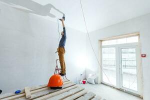 Builder worker with pneumatic hammer drill perforator equipment making hole in wall at construction site photo