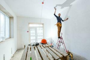 Thirty years old manual worker with wall plastering tools inside a house. Plasterer renovating indoor walls and ceilings with float and plaster. photo