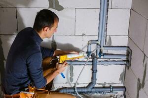 Young Male Plumber makes wiring of sewer pipes photo