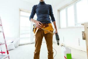 The builder in a protective helmet holds the professional puncher-hammer with a drill of the big diameter photo