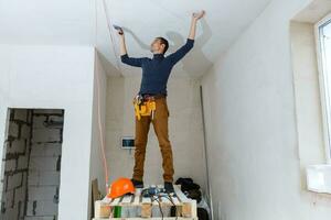 Thirty years old manual worker with wall plastering tools inside a house. Plasterer renovating indoor walls and ceilings with float and plaster. photo