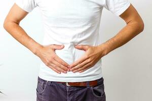 Young handsome man wearing white t-shirt over isolated background with hand on stomach because nausea, painful disease feeling unwell. Ache concept. photo