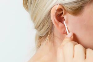 Middle aged woman cleaning her ear with cotton swab or stick. Closeup of hygiene healthcare routine procedure at home photo