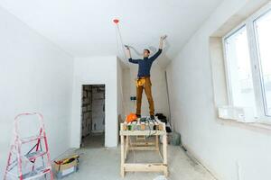 Trabajador manual de treinta años con herramientas de enlucido de pared dentro de una casa. yesero renovando paredes y techos interiores con flotador y yeso. foto