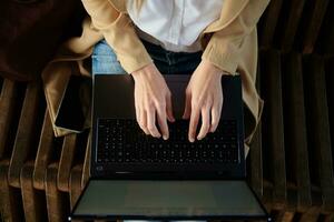Woman sitting on bench and typing on laptop keyboard photo