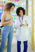 Happy young woman customer standing with lady pharmacist explaining drug details photo