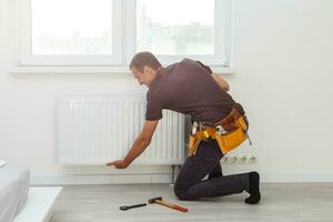 hombre es reparando radiador batería en el habitación. mantenimiento reparar trabajos renovación en el departamento. calefacción restauracion. llave inglesa en manos foto