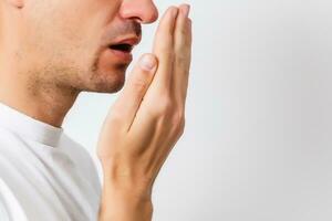 Bad breath. Halitosis concept. Young man checking his breath with his hand. photo