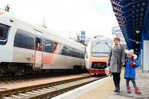 Yound woman and little girl, lovely daughter, on a railway station. Kid and woman waiting for train and happy about a journey. People, travel, family, lifestyle concept photo