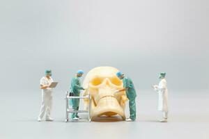 Miniature people Doctor with a giant human skull on a grey background photo