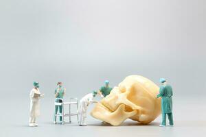 Miniature people Doctor with a giant human skull on a grey background photo