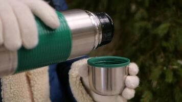 woman in mittens pours hot tea into cup in winter in mountains, hiking, rest and relaxation, slow motion tourist video