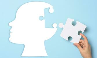 Silhouette of a human head holding a puzzle piece on a blue background, representing mental health photo