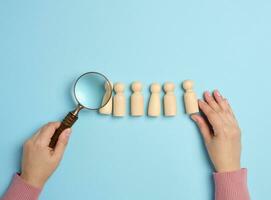 Wooden men and a magnifying glass on a blue background. Recruitment concept, search for talented and capable employees photo