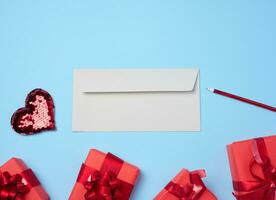 White paper envelope on a blue background, around a box with gifts, top view photo