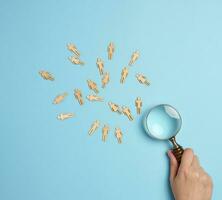 Wooden men and a magnifying glass on a blue background. Recruitment concept, search for talented and capable employees photo