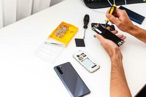 Repairman workplace with phone and special tools. Disassembled smartphone with disassembling instruments and repairer hands on white background. Electronics repair service, device production concept photo