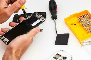 Repairman workplace with phone and special tools. Disassembled smartphone with disassembling instruments and repairer hands on white background. Electronics repair service, device production concept photo