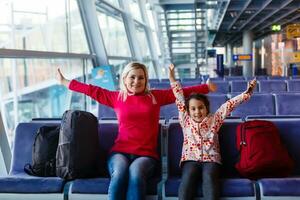 adorable niñito niña y su mamá esperando a el aeropuerto con equipaje, de viaje con niños, familia vacaciones, hora a el esperando habitación foto