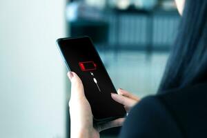 Close up view of woman holding smartphone with low battery symbol notification on the screen. Battery power and plugging the charger into your smartphone with a power backup charger photo