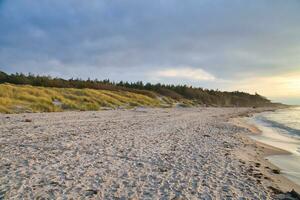 Sunset on the west beach on the Baltic Sea. Waves, beach, cloudy sky and sunshine photo