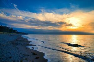 Sunset on the west beach on the Baltic Sea. Waves, beach, cloudy sky and sunshine photo