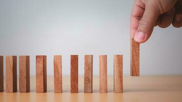 Businessman hand stopping falling blocks on table, stopping the domino effect concept for business solution, strategy and successful intervention. photo