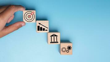 Human hands hold wooden blocks with target icons and business symbols on blue background, business goals and objectives concept, business competition. photo