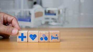 salud y médico concepto humano mano sostiene un de madera bloquear con íconos acerca de salud y acceso a tratamiento y medicina y suministros en un azul antecedentes. foto