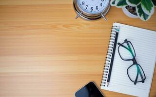 Office table of modern workplace with notebooks and pencils, phone, clock on wooden table. Top view and copy space on wooden floor, Flat lay, top view office table with glasses. photo