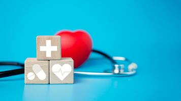 The concept of health insurance and medical welfare. Block wooden and red heart with plus icon. Health insurance and access to health care. photo