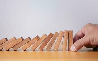 Businessman hand stopping falling blocks on table, stopping the domino effect concept for business solution, strategy and successful intervention. photo