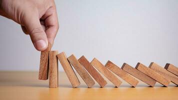 Businessman hand stopping falling blocks on table, stopping the domino effect concept for business solution, strategy and successful intervention. photo