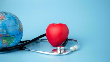 Concept of health insurance and medical welfare, model globe and red heart with stethoscope on blue background, health insurance and access to healthcare. photo