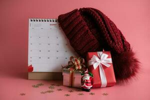 regalo caja y calendario con un rojo de punto lana sombrero en rosado antecedentes. navidad día concepto. planificación Planificación agenda, evento, organizador Navidad día. foto