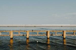 Yellow fence in cold sea water of Baltic with a grey pier on the background photo