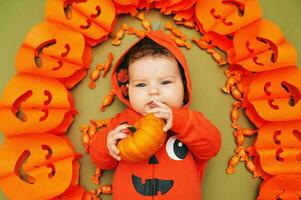 Halloween portrait of adorable baby lying on green background next to pumpkin garland photo