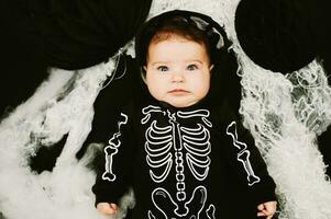 Halloween portrait of adorable baby wearing skeleton costume, posing on black background covered with spider web photo