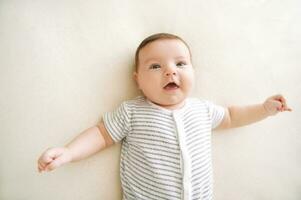 Portrait of adorable 6 months old baby lying on on white couch, happy facial expression photo