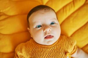 Portrait of adorable 6 months old baby lying on yellow play blanket photo