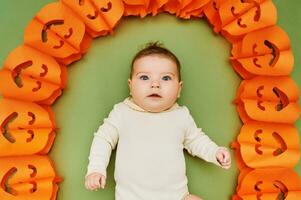Halloween portrait of adorable baby lying on green background next to pumpkin garland photo