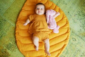 Portrait of adorable 6 months old baby lying on playing blanket, holding pink bunny toy, top view photo