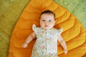 Portrait of adorable 6 months old baby lying on yellow play blanket photo