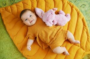 Portrait of adorable 6 months old baby lying on playing blanket, holding pink bunny toy, top view photo