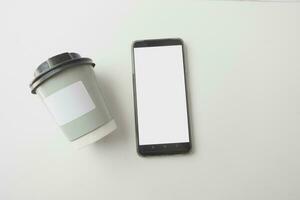 Blank take away kraft coffee cup and smart phone with empty screen photo