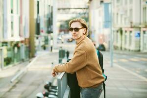 Outdoor portrait of handsome young man wearing sunglasses and beige fuzzy fleece sweater, posing on city street background photo