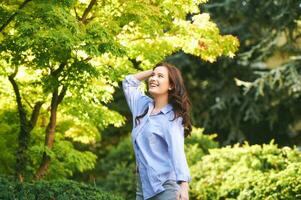 al aire libre retrato de contento joven mujer disfrutando ambiente en verde parque foto