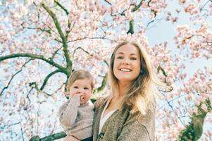 Outdoor portrait of happy young mother with adorable baby girl under blooming spring tree, bottom view photo