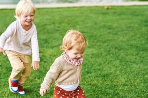 Outdoor portrait of adorable happy children playing together, running after each other, siblings love photo