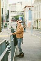 al aire libre retrato de hermoso joven hombre vistiendo Gafas de sol y beige borroso lana suéter, posando en ciudad calle antecedentes foto